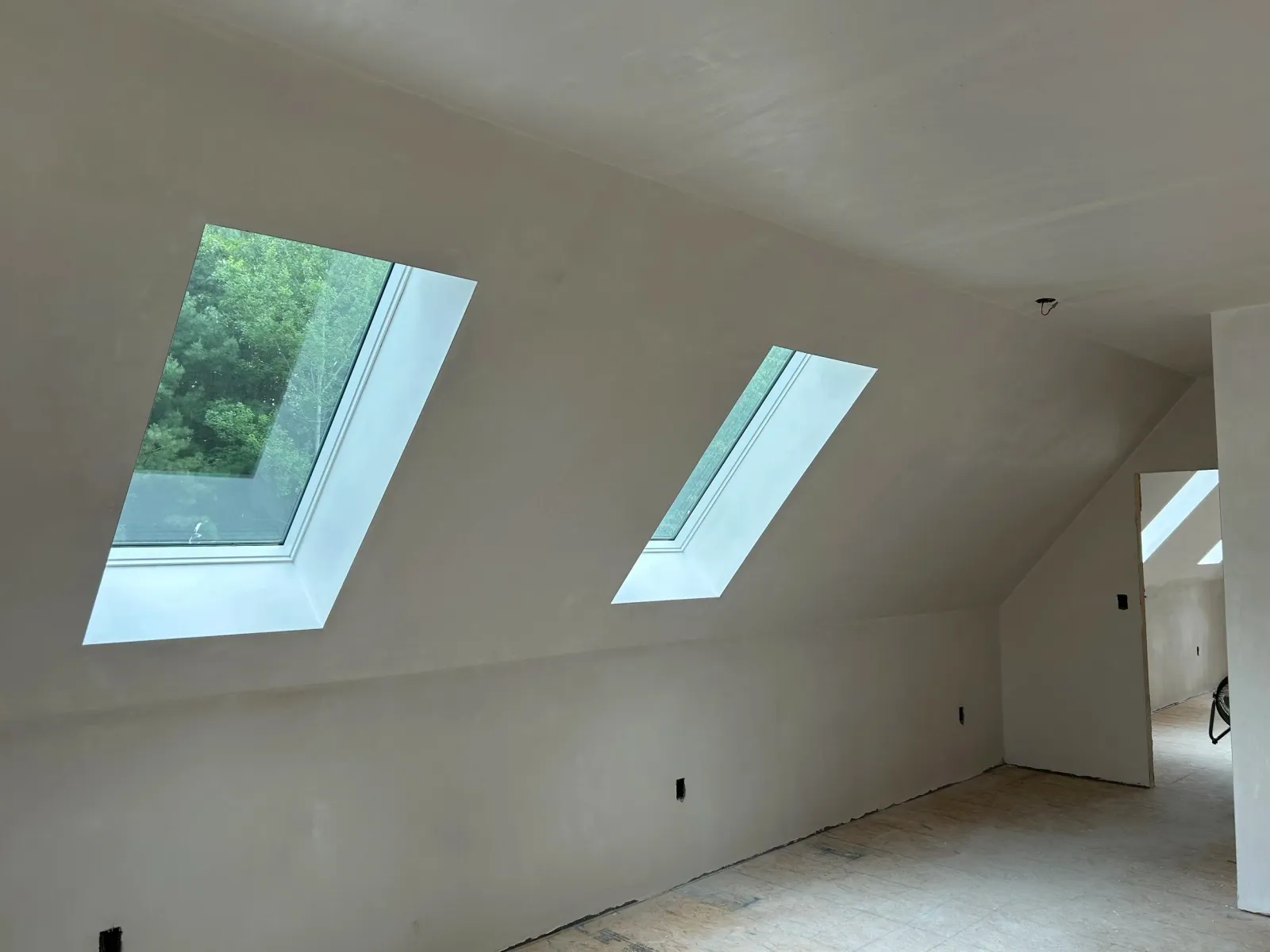 Empty room with sloped ceiling and three skylight windows, under construction or renovation.