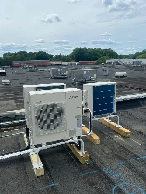 Rooftop with HVAC units and equipment, wooden support beams, and a view of green trees and a partly cloudy sky in the background.