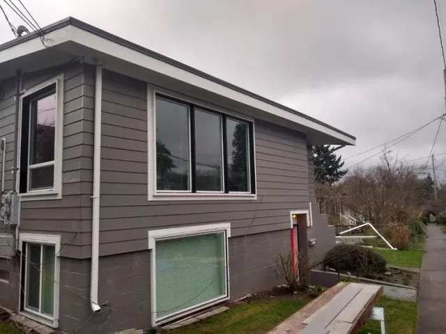 Crisp Gray two-story house exterior with large windows, overcast sky, and a small fenced yard