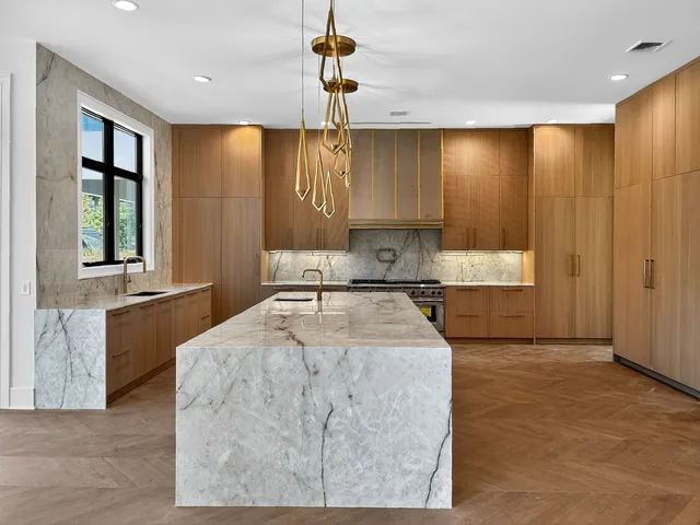 Luxury new-build kitchen with a veined stone island, warm wood cabinetry and brass-toned pendant lighting