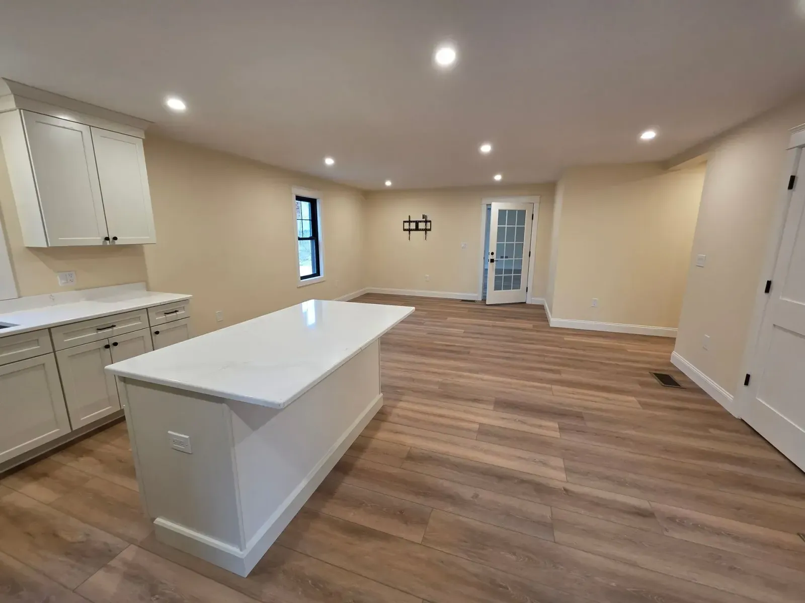 Open-concept kitchen with white cabinets, island, and wood-look flooring. Neutral walls, recessed lighting.