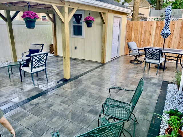 Backyard patio with pergola, paver flooring, and seating area, designed by Perfect North Lawn Care in New Hampshire.
