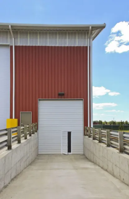 Warehouse entrance with red and white siding, white garage door, and concrete ramp.