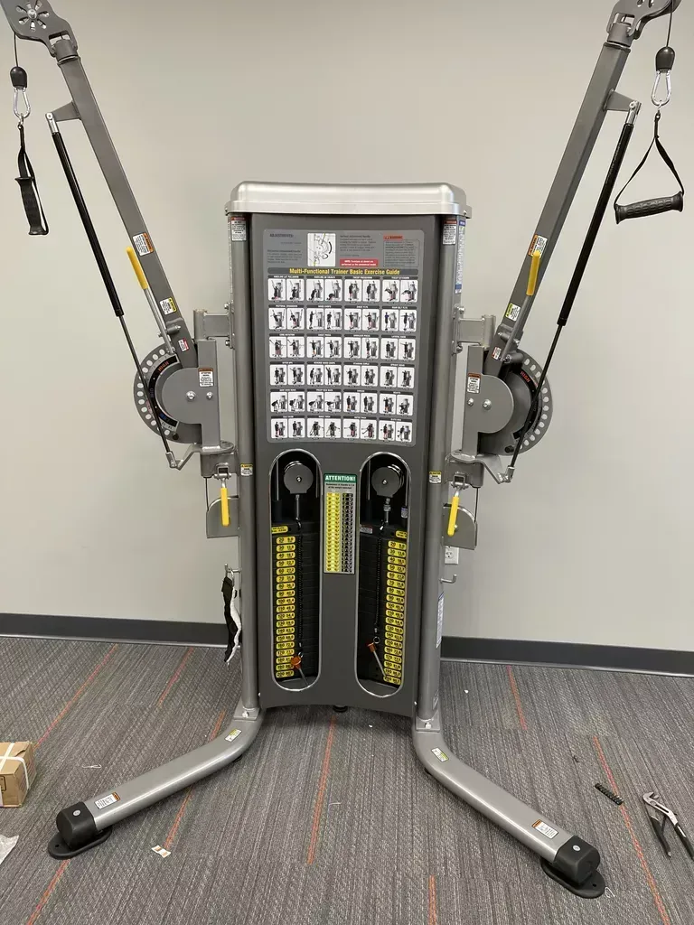 Gym cable machine with yellow weight stacks and multiple pulleys in a workout room
