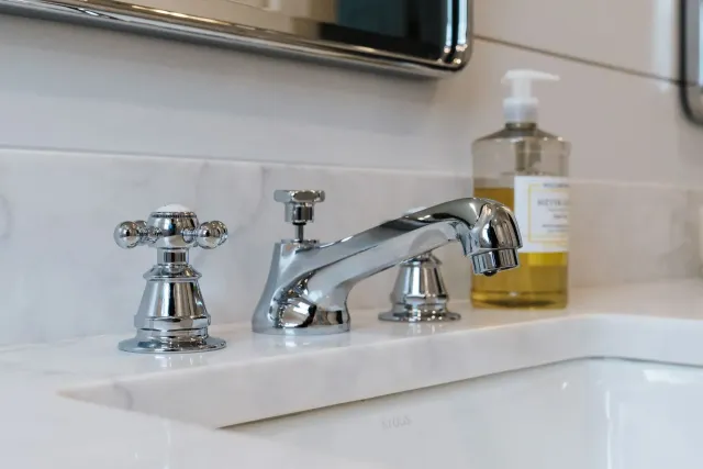 Chrome bathroom sink faucet with soap dispenser on a white countertop