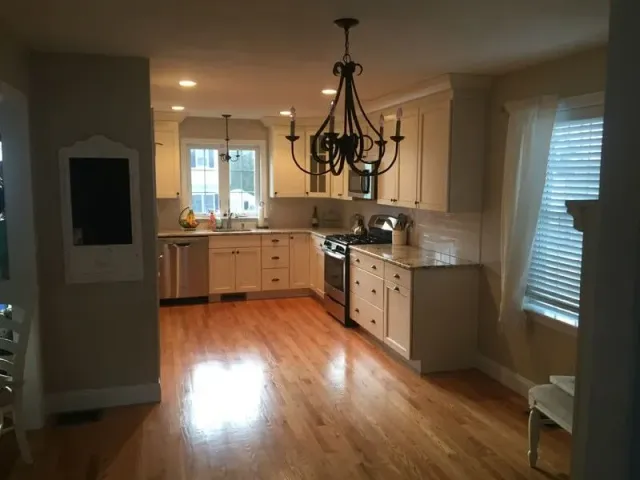 Kitchen with wood floors, light cabinets, stainless steel appliances, and a chandelier.