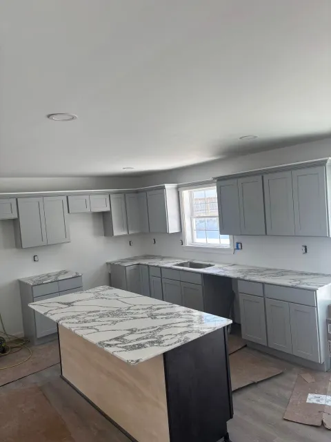Kitchen with gray cabinets, white countertops, and an island in a bright, unfinished room.