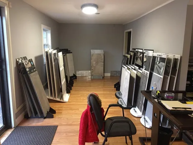 Room with many folded screens, a chair, desk, and coat; light hardwood floors, gray walls.