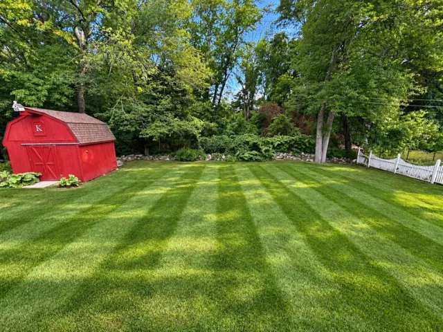 Red barn on manicured lawn with alternating stripe pattern, surrounded by mature trees and white fence