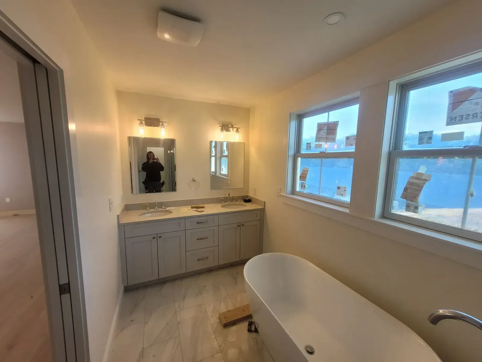 Bathroom with vanity, mirrors, windows, and a soaking tub. Light gray cabinets and flooring.