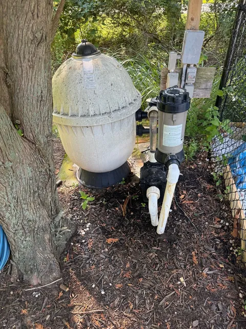 Old, weathered sand filter and pump beside a tree