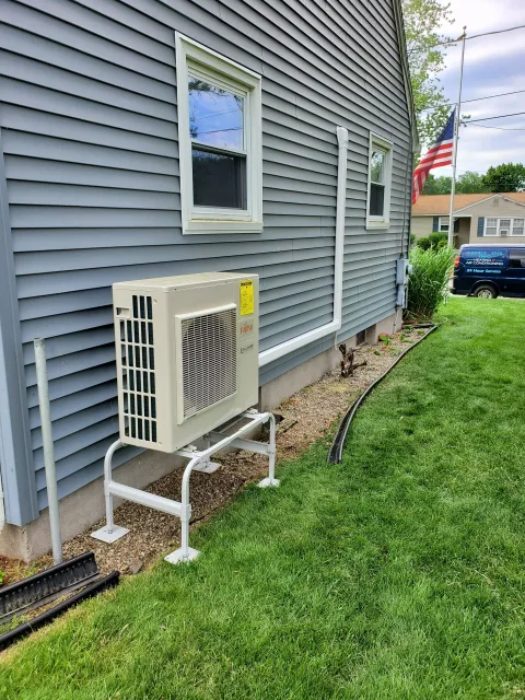 Exterior view of a gray house with a mounted air conditioning unit on a metal stand.