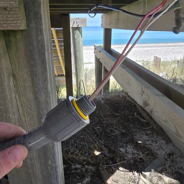 Weatherproof conduit fitting installed beneath a beach house deck