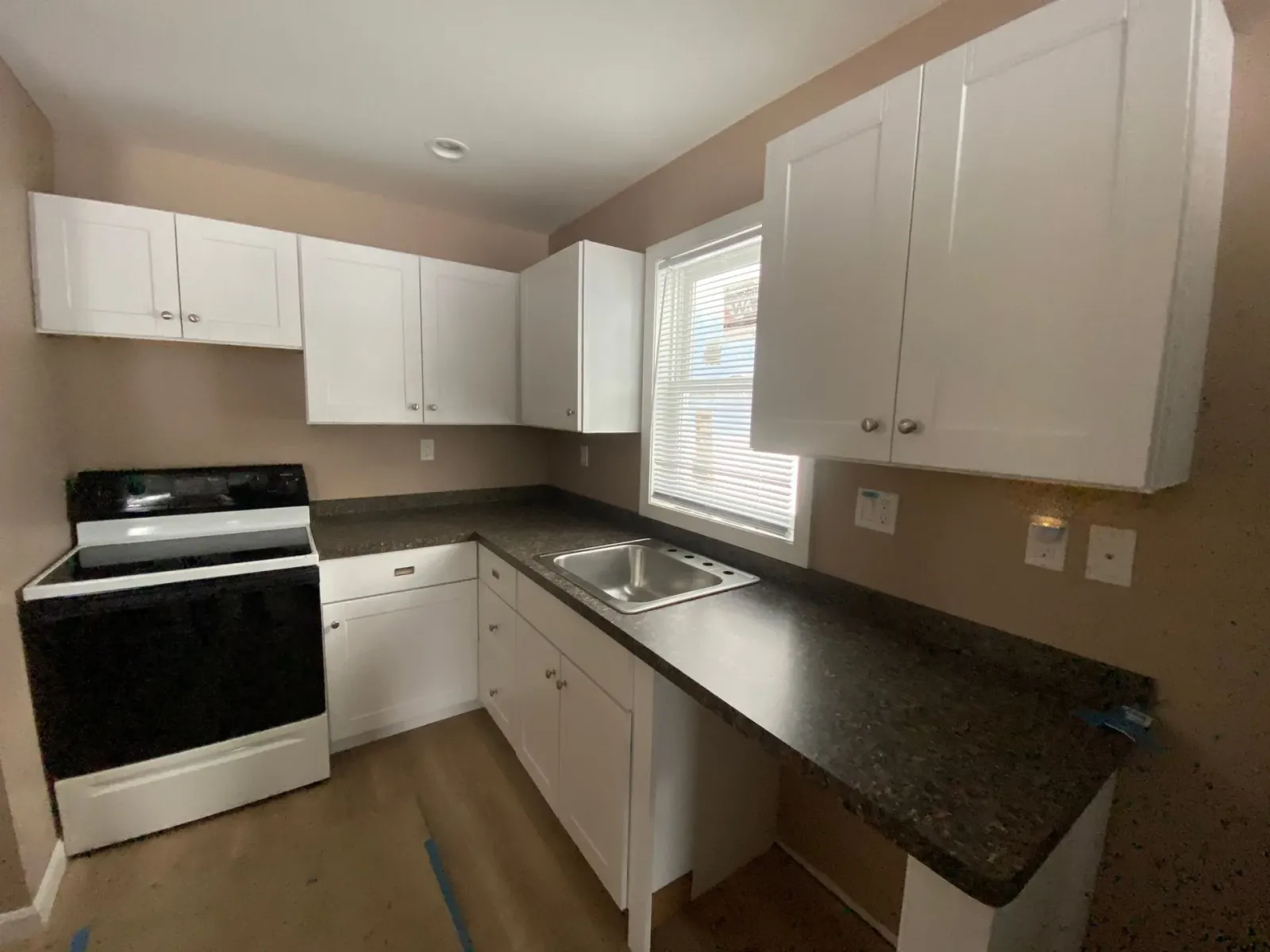 A kitchen with white cabinets , a black stove , a sink and a window.