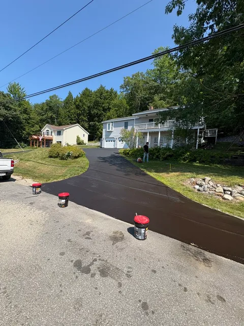 Sealcoating in progress on a sloped residential driveway with buckets of sealer at the road