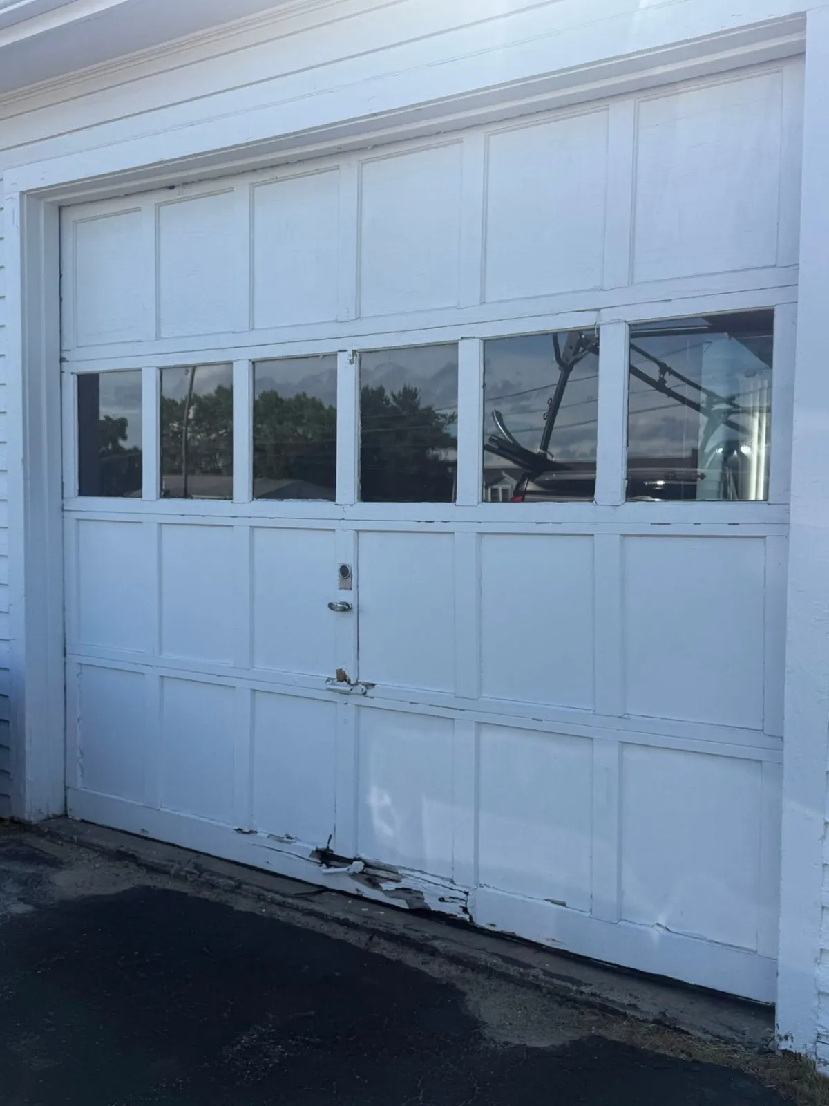 Aging white wooden garage door with damaged bottom panel before replacement