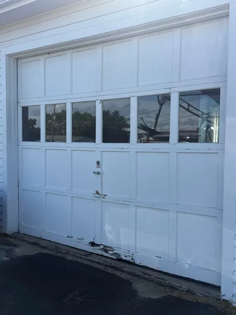 Aging white wooden garage door with damaged bottom panel before replacement