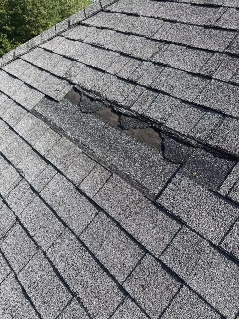 Close-up of a roof with asphalt shingles, showing damage and a damaged section with missing or displaced shingles.
