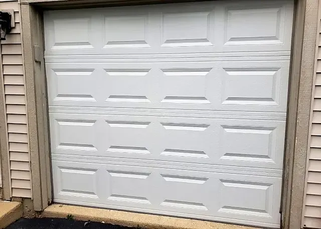 White raised-panel single garage door set in beige siding