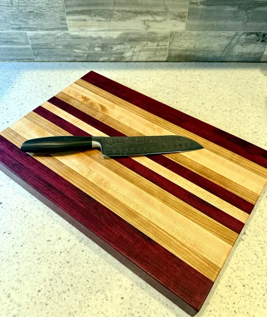 Handmade cutting board of alternating purpleheart and maple stripes with a chef's knife resting on it