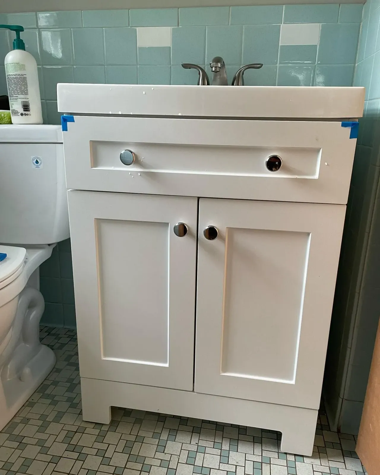 White bathroom vanity with sink and double cabinet doors next to a toilet and tiled wall.