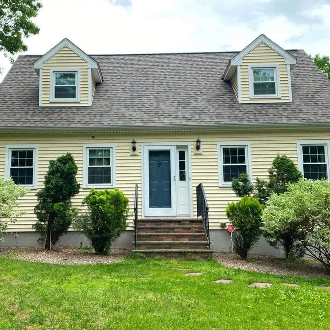 Yellow-two-story-house-with-dormer-windows,-dark-roof,-and-blue-front-door