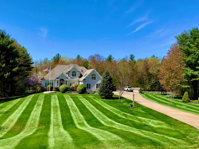 Immaculately striped front lawn of a residential property with lush green grass, maintained by Perfect North Lawn Care in New Hampshire.