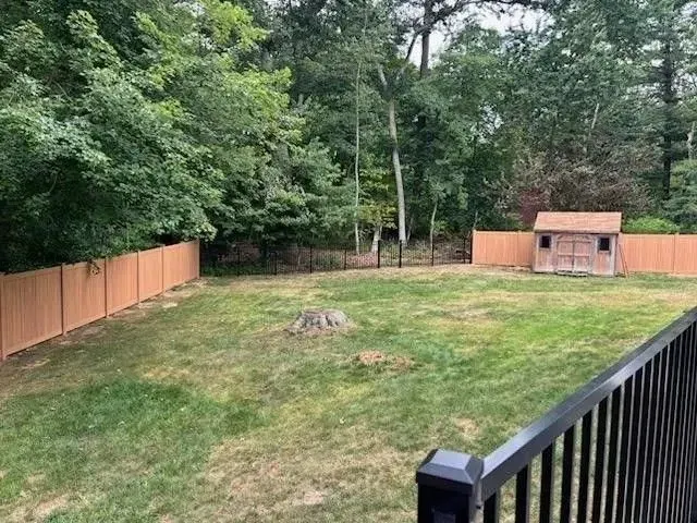 Backyard with green lawn, wooden fence, trees, and a small shed