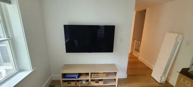 Minimal living room with wall-mounted TV, white media console, and a bright window on the left.