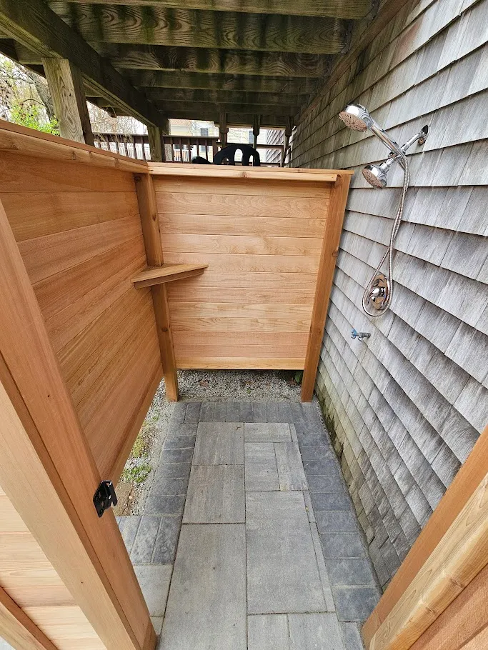 Clear cedar outdoor shower with louvered privacy wall and bluestone paver floor in Saunderstown, Rhode Island by Toensing Construction