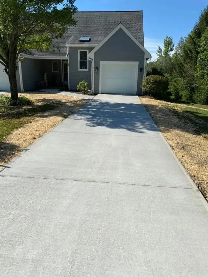 Gray concrete driveway leading to a gray house with a white garage door on a sunny day.
