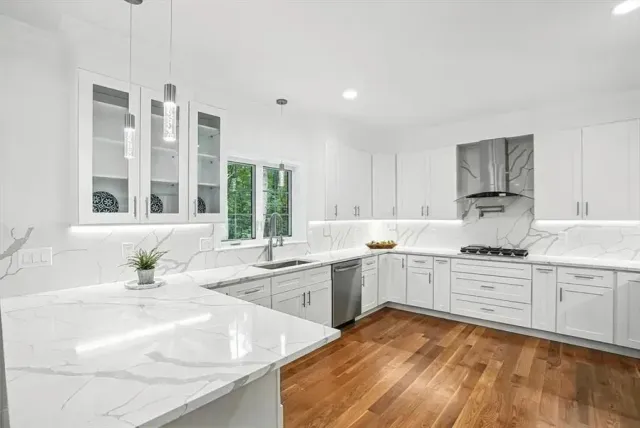 White kitchen with marble countertops, stainless steel appliances, and wood flooring.