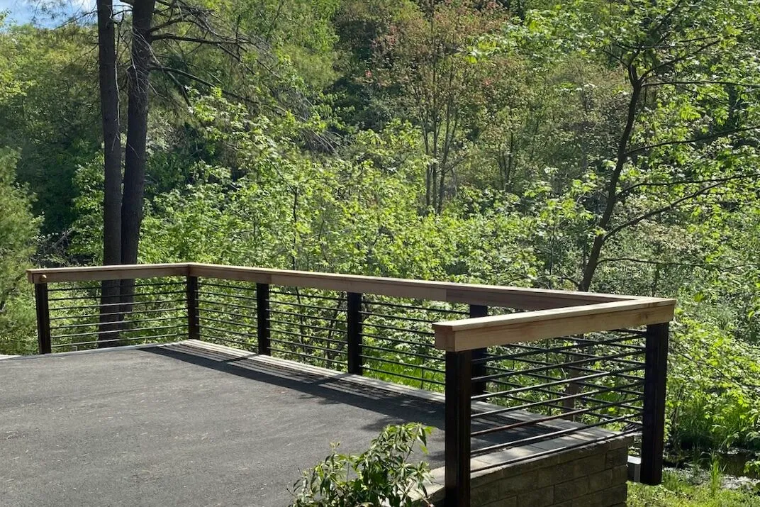 high-end landscape design and general contracting boston: Attractively rusted Corten Steel & cedar railing surrounds the end of a driveway looking over a sheer dropoff with a beautiful view of New England forest.