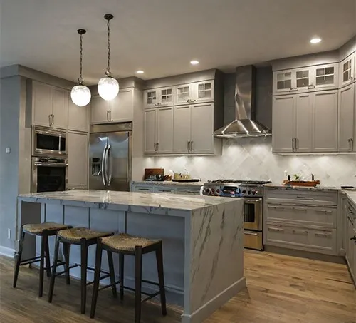 Modern kitchen with gray cabinets, stainless steel appliances, a marble island with stools, and pendant lights.