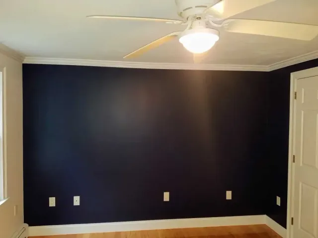 Dark blue accent wall in a room, with white trim, a ceiling fan, and electrical outlets.