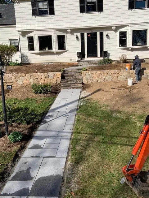 Front walkway leading to a house entrance, with stone steps, lawn, and construction equipment on the right.