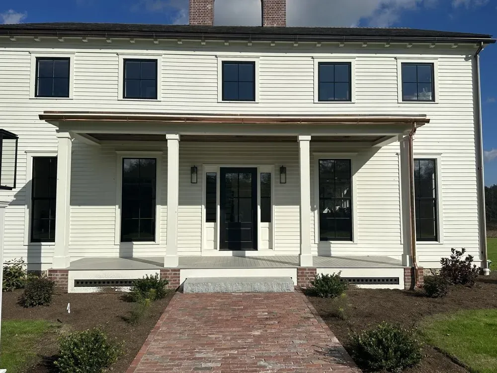 White two-story house with black trim, a front porch, and a brick walkway leading to the entrance