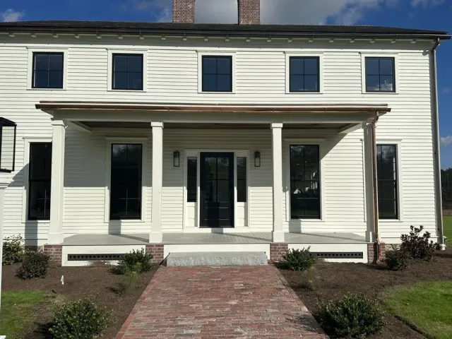 White two-story house with black trim, a front porch, and a brick walkway leading to the entrance