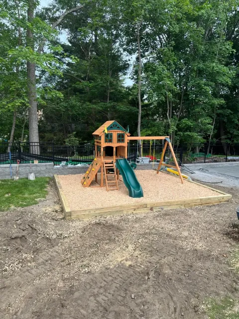 Children’s playground with orange-and-green slide set on a sand base in a wooded park.
