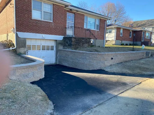 Brick house with garage and sloped driveway beside a retaining wall in a suburban neighborhood