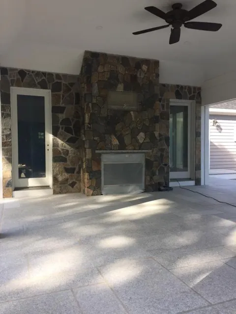 Outdoor patio area with stone fireplace, sliding glass door, ceiling fan, and concrete floor.