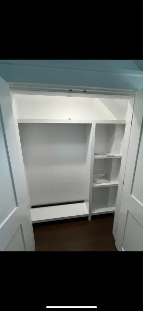 Empty walk-in closet with white shelving units, built-in storage and dark wood flooring