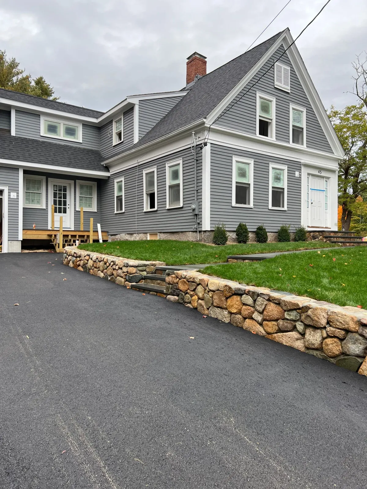 A large gray house with a stone wall in front of it.