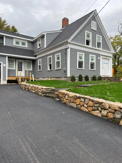 A large gray house with a stone wall in front of it.