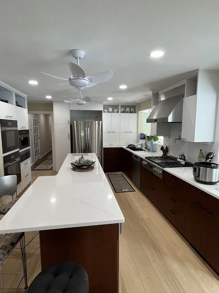 dual modern white ceiling fans and recessed lighting installed in a kitchen with a long white marble island