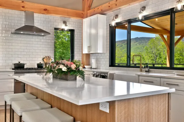 Killington kitchen with a pale stone island, white cabinetry and mountain views beneath exposed timber beams.