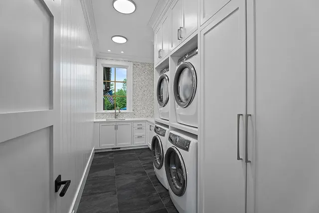 White laundry room with washer, dryer, cabinets, dark tiled floor, and a small window.