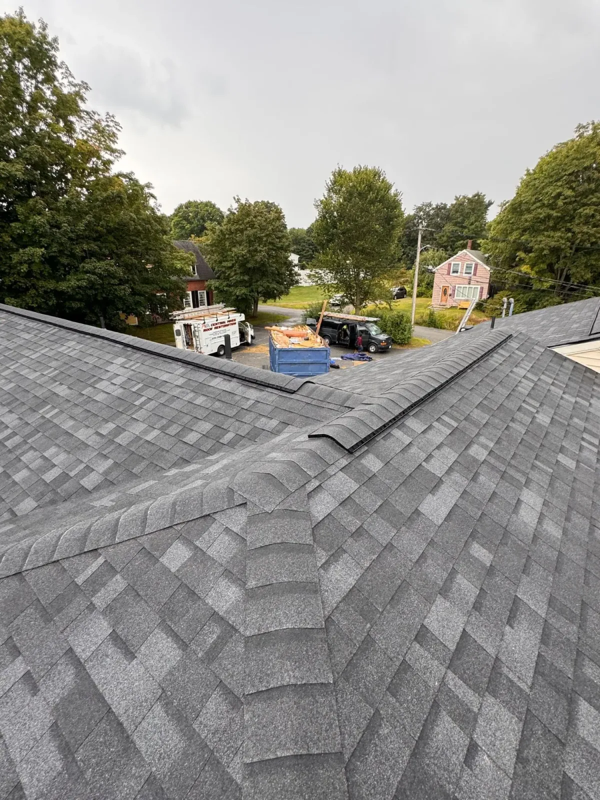 Gray shingle roof overlooking trees, parked vehicles, and houses under an overcast sky