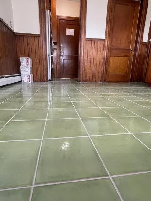 A room with green tiled floor, wooden wall paneling, and multiple doors, including a main entrance door in the background.