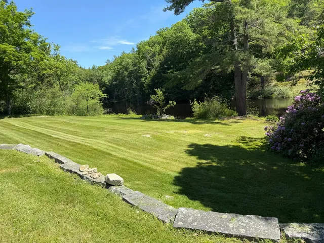 A freshly mowed, striped green lawn beside a wooded pond, maintained by S.K. Lawn Care